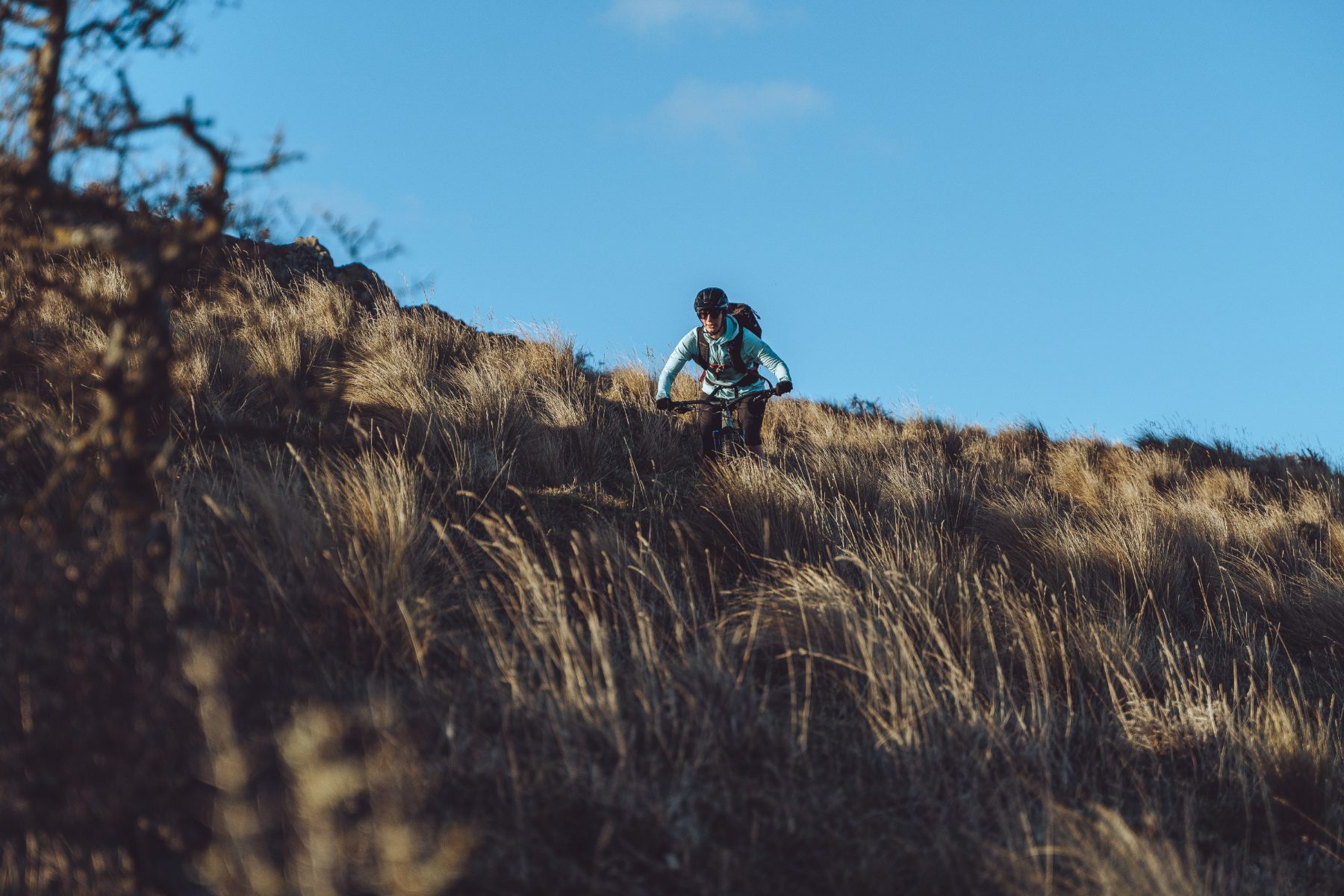 Mountain biker climbing a tussock ridgeline in the Canterbury high country on a Ride Sherpa MTB shuttle day